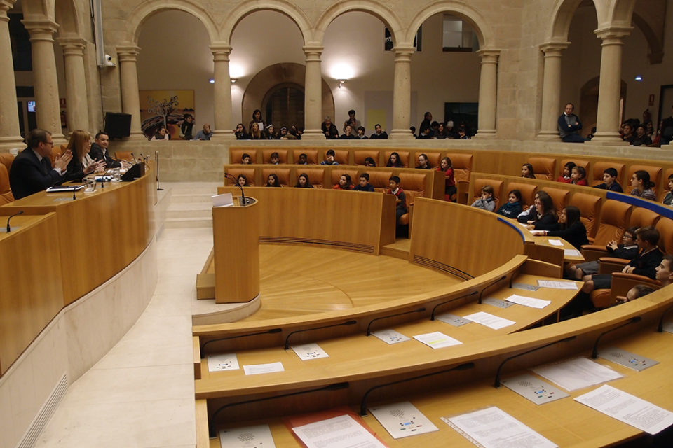 Los escolares ocupan los escaños del Parlamento riojano, donde han leído los artículos de la Constitución. / NR